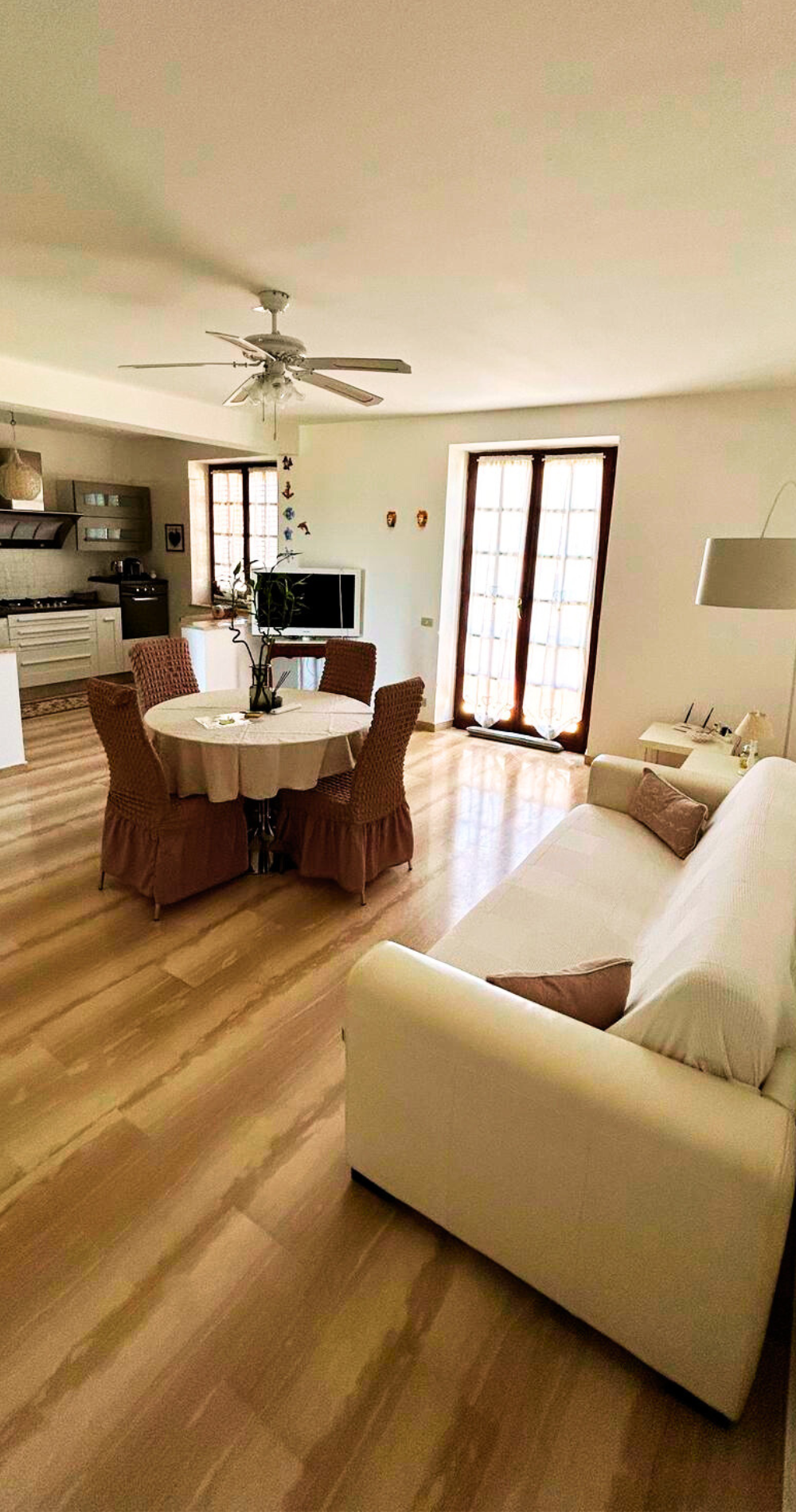 Interior da sala de estar da cobertura Sinus Felix em Terrasini com mesa de jantar em madeira e sofá moderno, inundada de luz natural